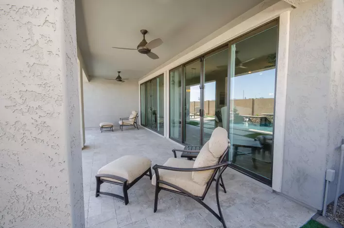 A large back patio with lounge chairs that is on the back of a gray home with an entire wall of sliding patio doors.