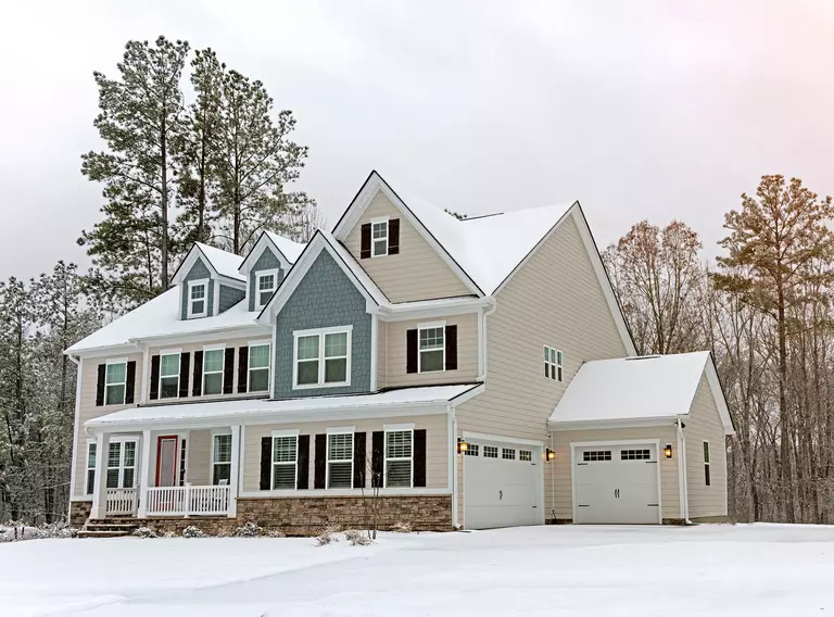 Snow-covered house with two white wood garage doors.