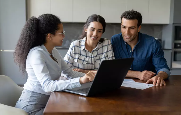 Couple sitting at a desk with a home improvement consultant as they look at a laptop in front of them.