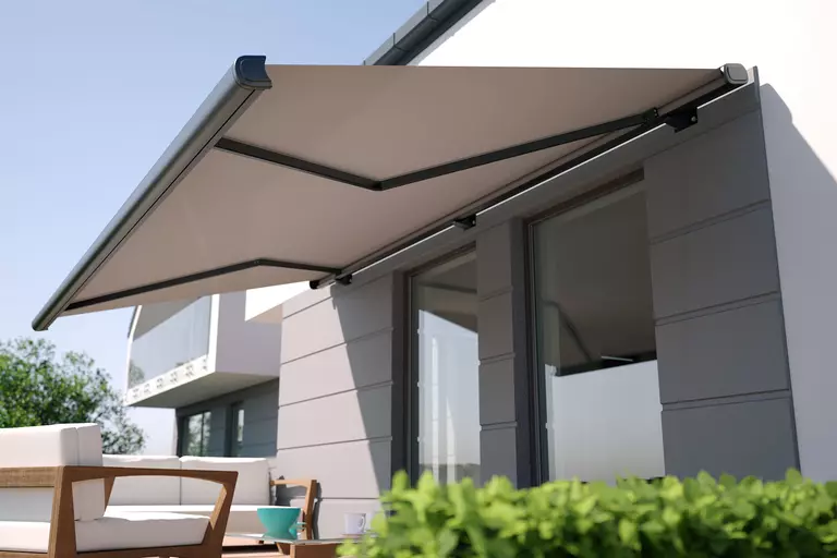 The outside of a home with an awning covering two windows and an outside seating area.