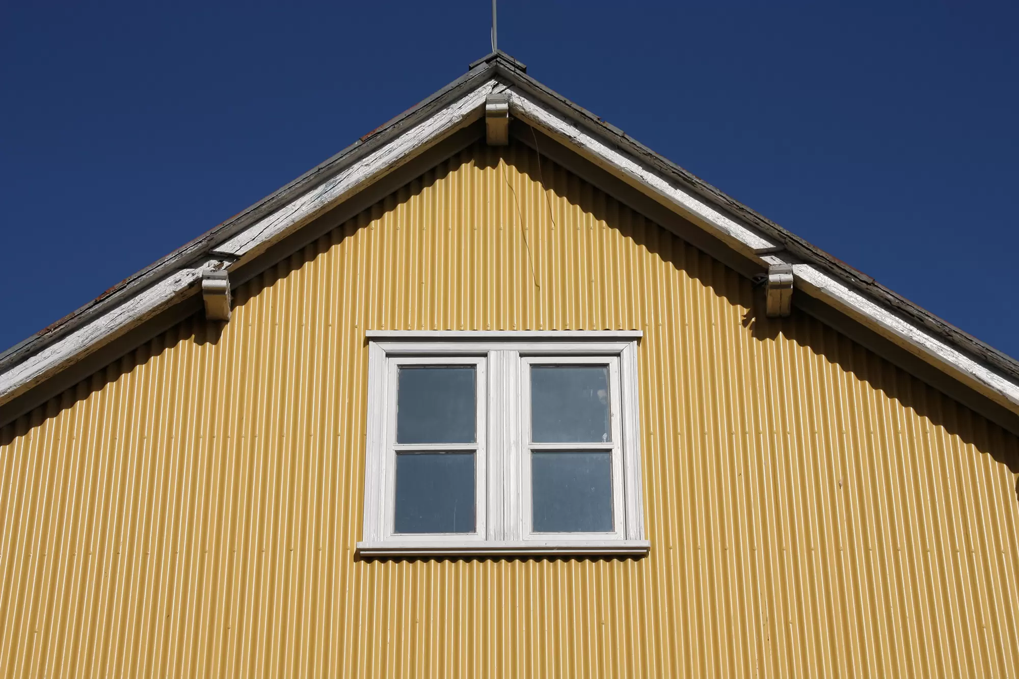 Yellow corrugated metal siding on a home gable with a white-framed window.