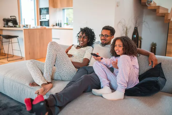 A husband and wife sitting on their couch watching TV with their daughter in a cozy
living room.