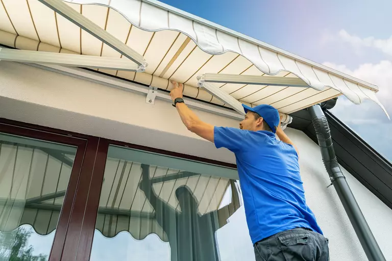 A man installs exterior window awnings to help prevent the sun from heating up a house.