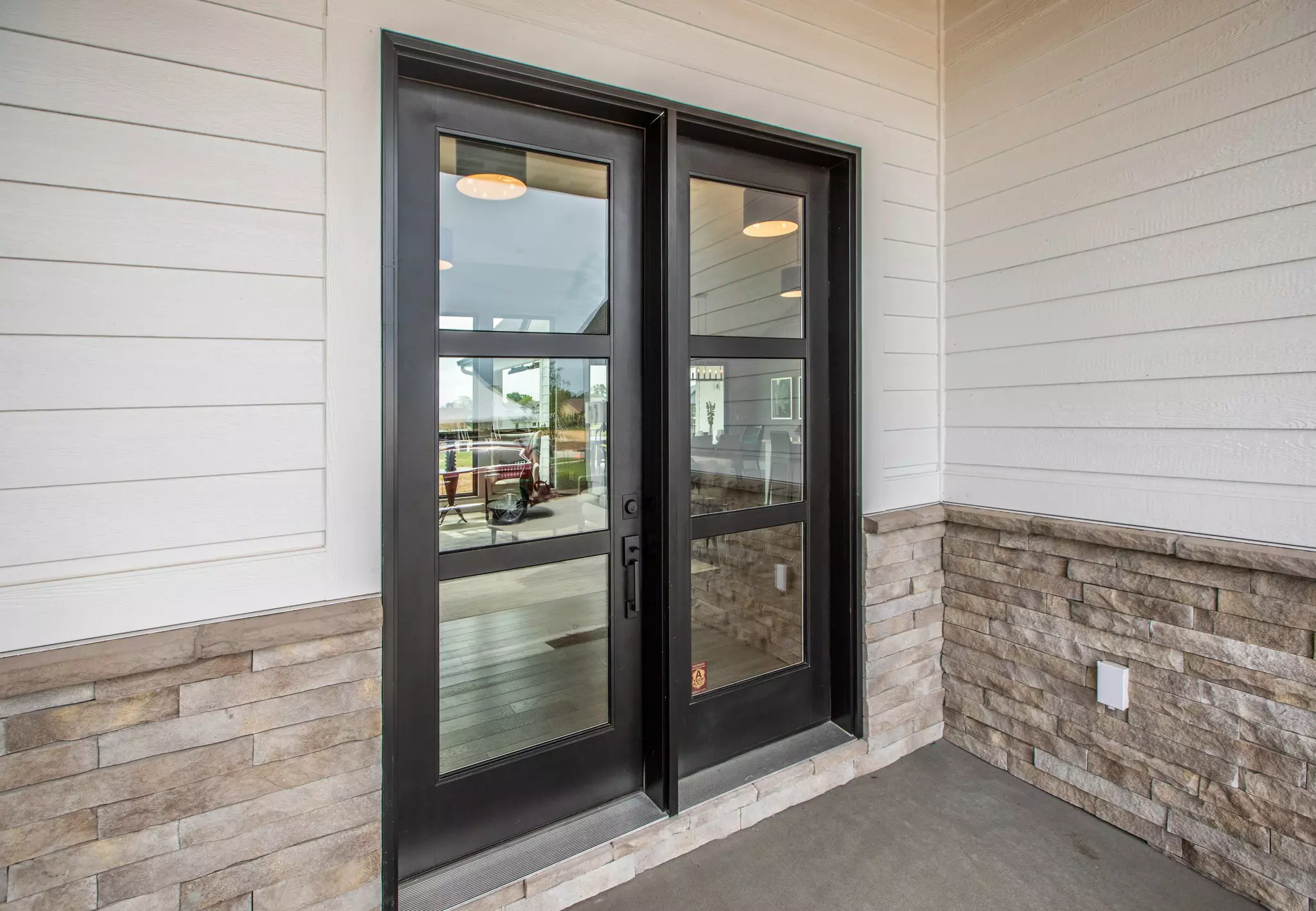 Black hinged patio door on a home with white siding and stone.
