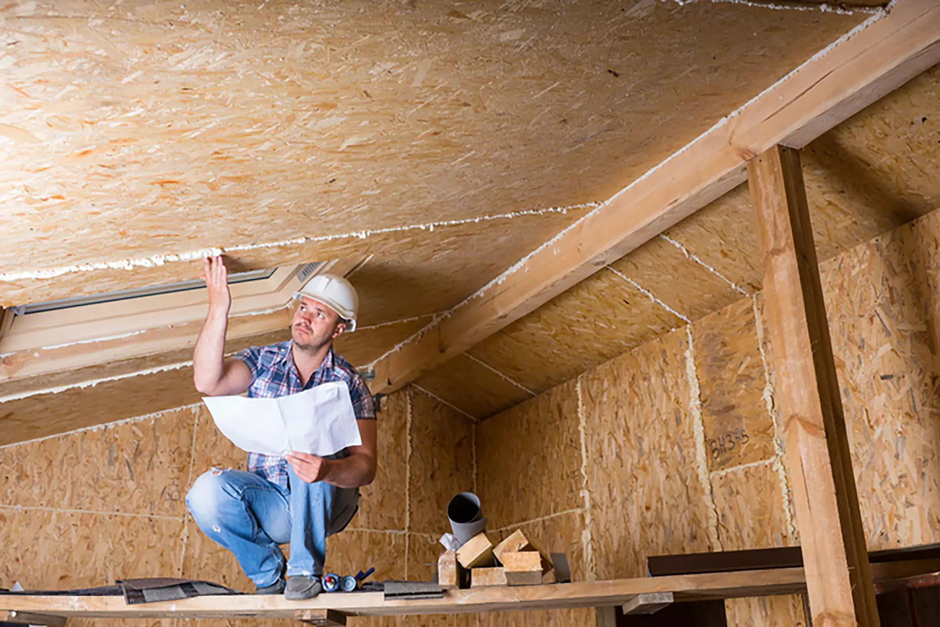 A contractor performs routine roof maintenance by checking for leaks in an attic.