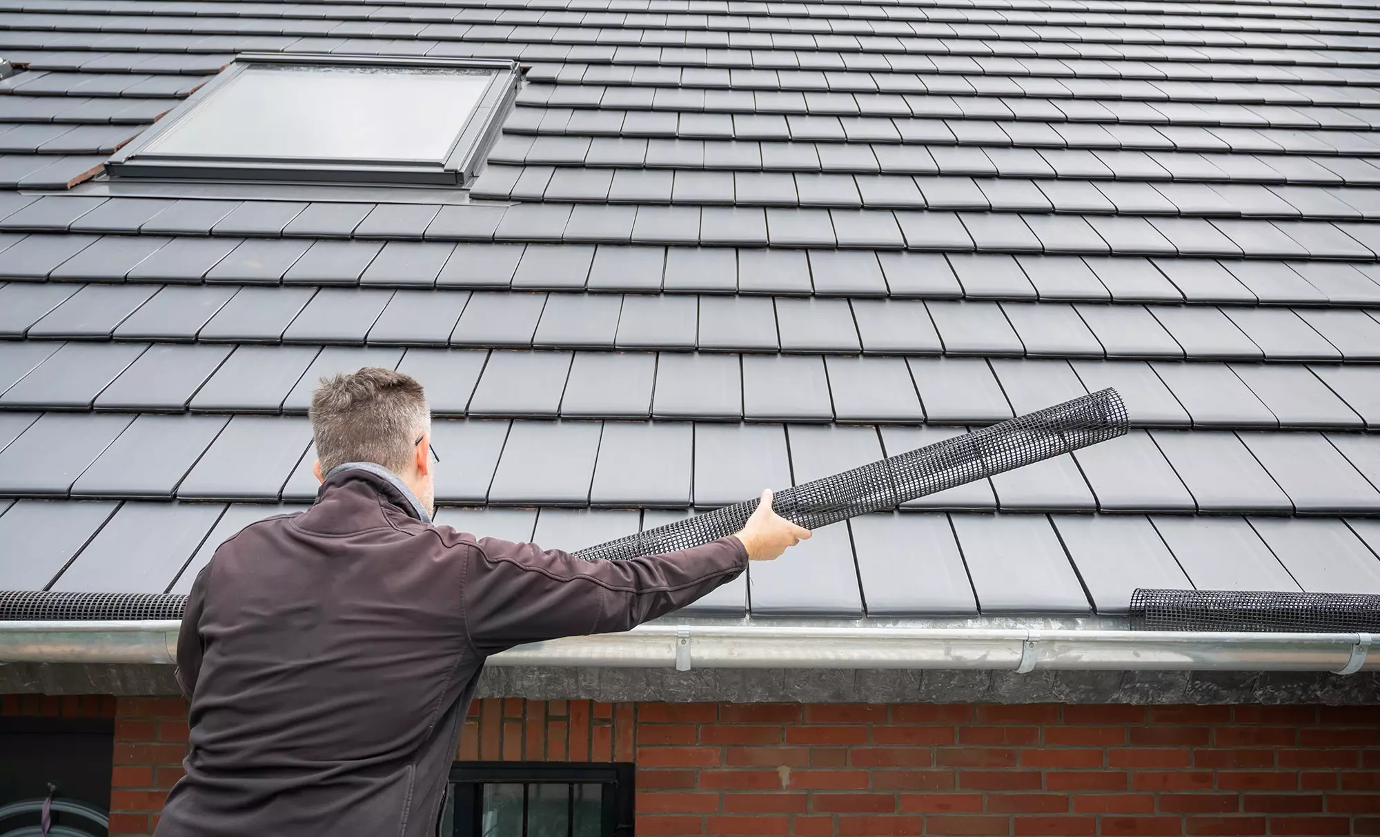 A man installing a gutter guard into the gutter system of a home to prevent dirt, gunk, and other debris from entering.