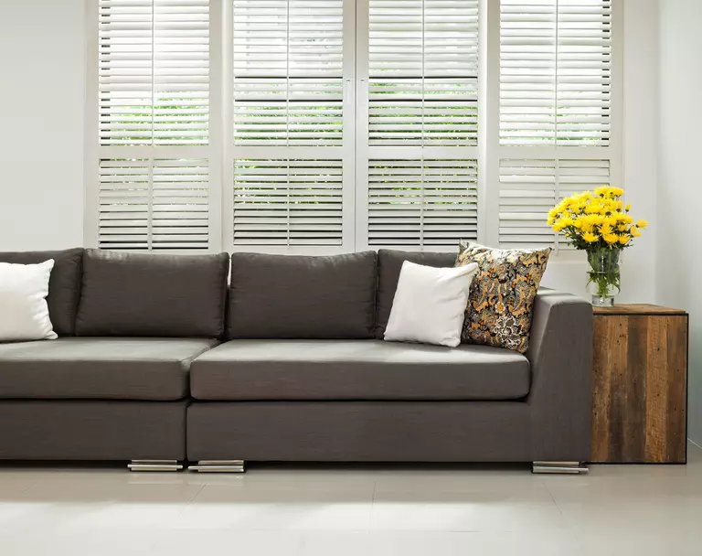 Living room of a home with a gray couch in front of living room windows dressed with interior window shutters.