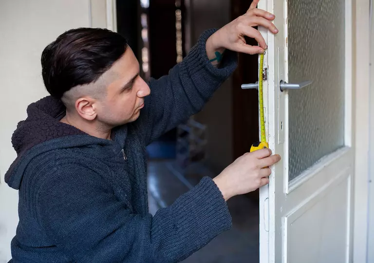 A man using a tape measure against a storm door.