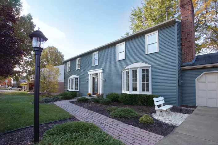 A home with blue siding, a brick chimney, two bow windows, and a landscaped yard that contains a light post.