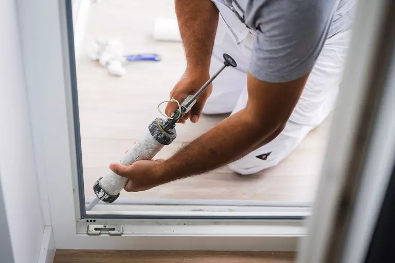 A worker applies caulk to the bottom corner of a glass patio door.