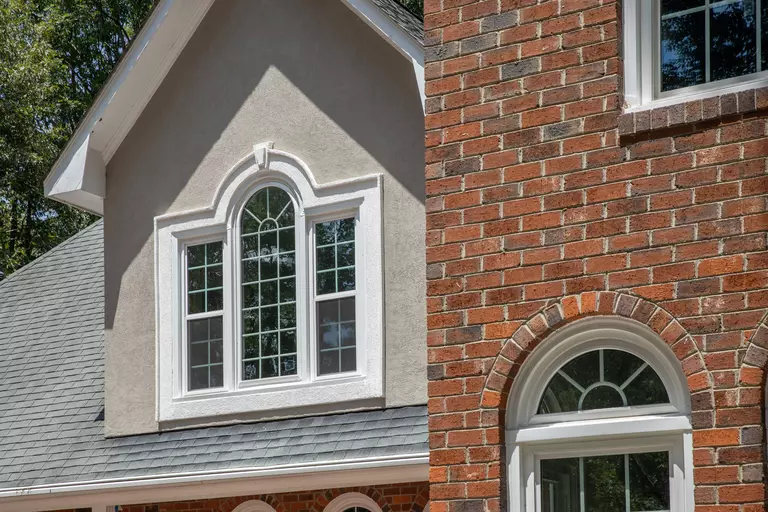 The exterior of a brick house, with several specialty shaped windows.