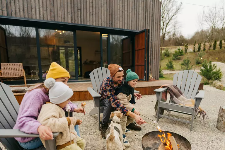A family roasting marshmallows together on their back patio that they have decorated with furniture, a firepit, lights, and landscaping.