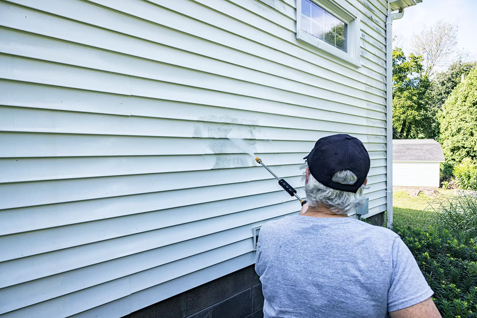 Man cleans vinyl siding of house with a pressure washer.