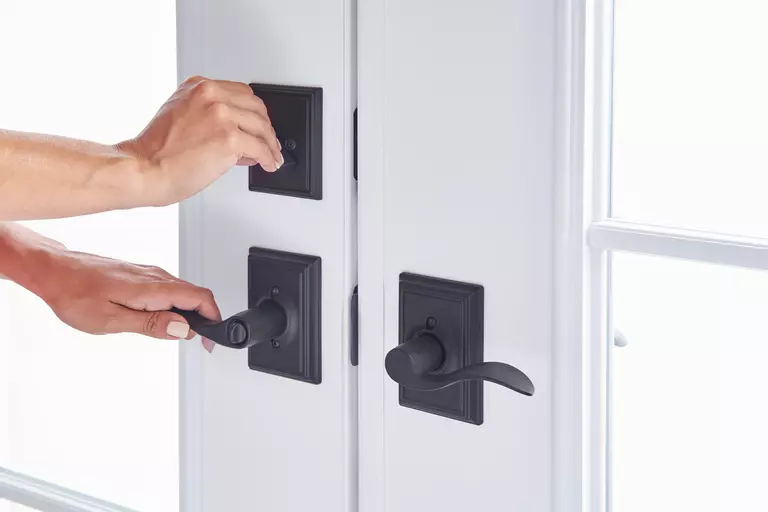 A closeup of a person deadbolting a set of two doors.