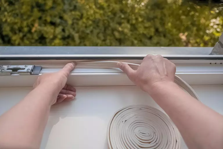 Individual applying weatherstripping to the edges of a window frame.