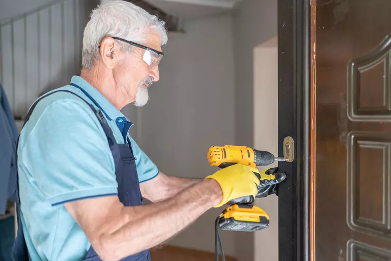 A worker uses a handheld drill to attach exterior door hinges.