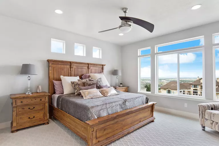 A large, clean bedroom with a gorgeous view overlooking nearby homes. The ceiling fan can be used to help circulate cooler air through the room.