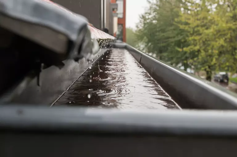 Closeup along the roof edge of a home with a pool of water accumulated in a gutter trench.