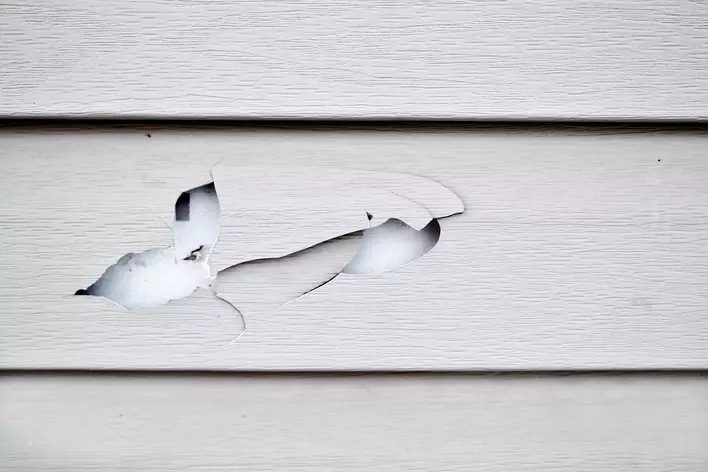 Close-up of a hole in the vinyl siding of a home