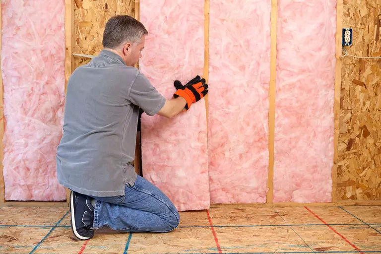 Man inserting insulation between gaps in a wall.