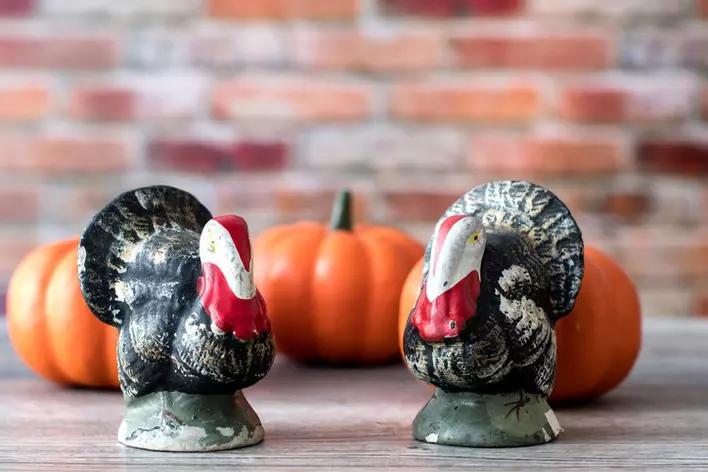 Two small turkey figures set up on a table next to three small orange pumpkins.