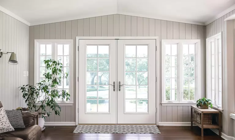 Entrance to a home with white hinged patio doors and casement windows with grids.