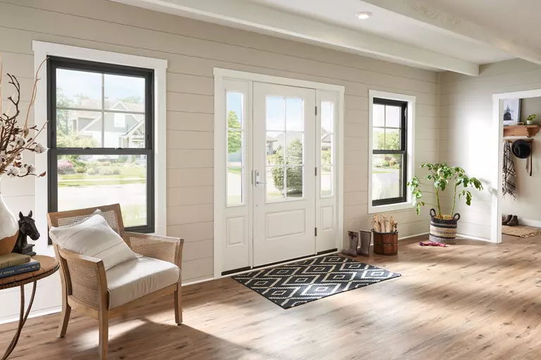 The front entryway of a home with black, double-hung windows and a white exterior door with sidelites.