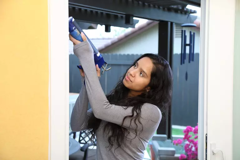 Woman using a caulking gun during an exterior door installation 