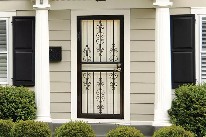 An ornate black storm door on the entryway of a home with decorative columns.