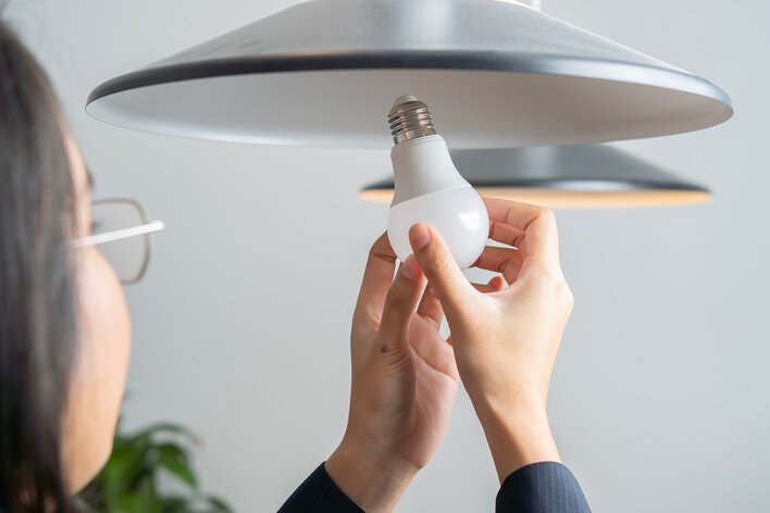 Person replacing lightbulb in the home and inputting an LED light to better reduce electric bills during winter.