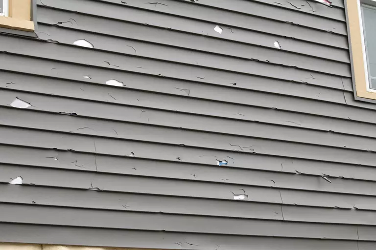 Close-up of damaged gray vinyl siding on a home.