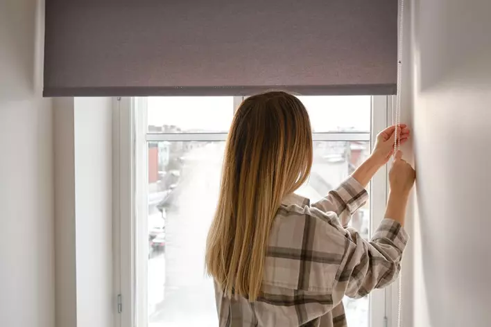 A woman inside, opening her roller blinds, uncovering a beautiful large window.