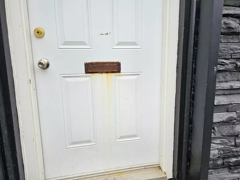 An old and stained exterior door with a rusting mail slot.