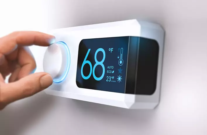 A person adjusts the setting on their thermostat to address a buildup of condensation
            inside windows in their home.