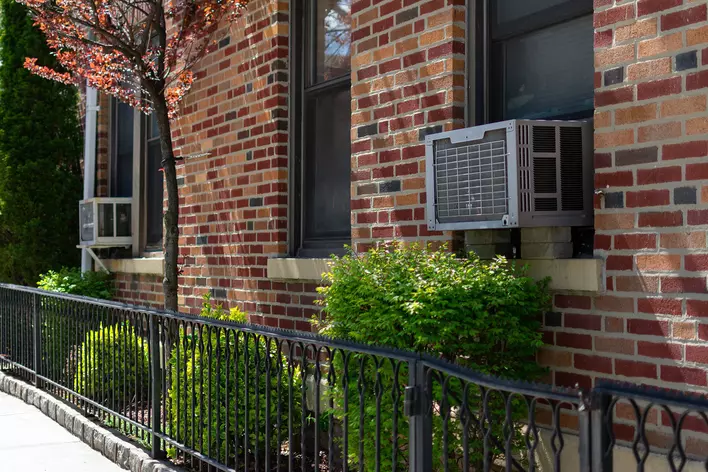 A brick building with window AC units on the side and a black fence in front