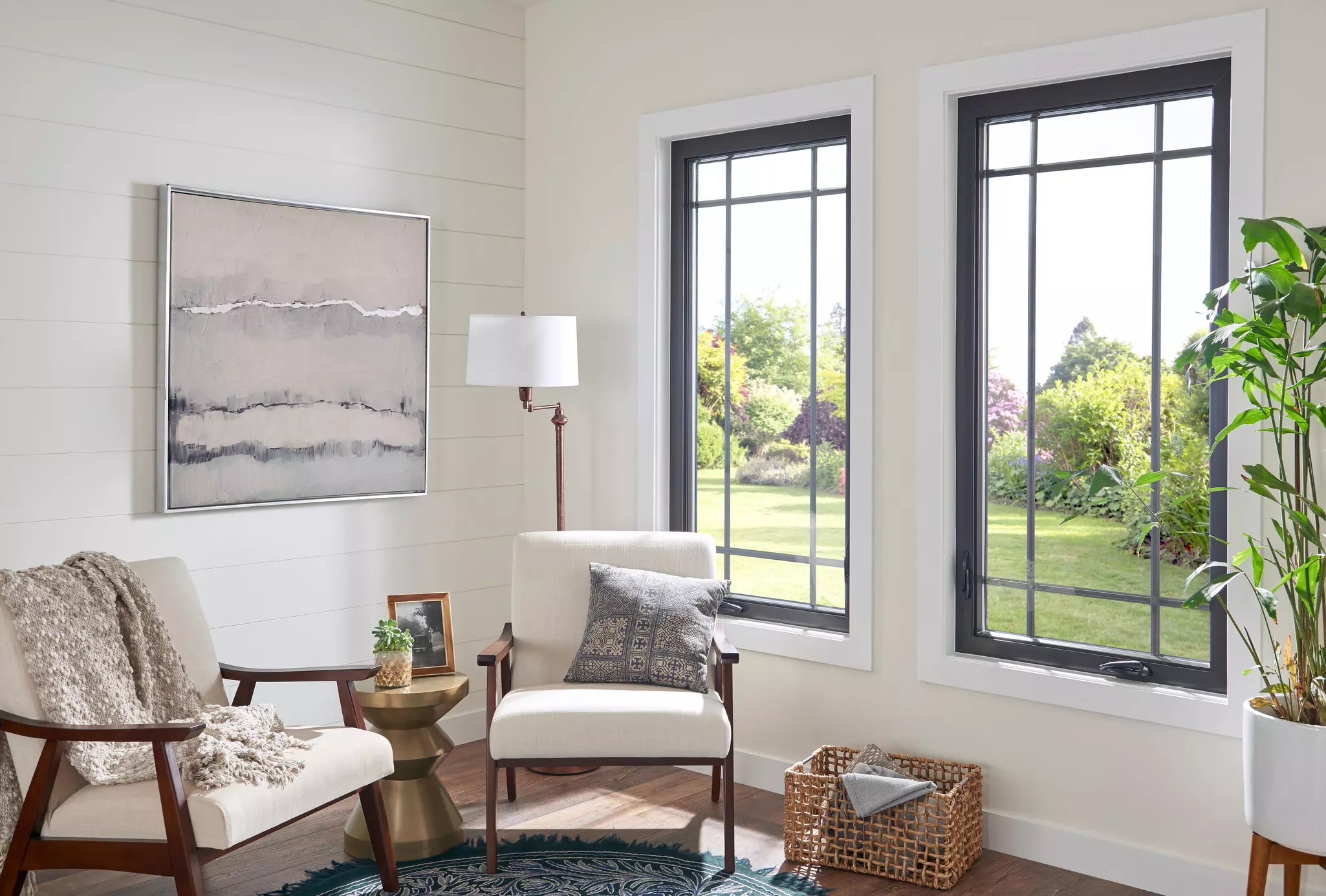 Two chairs in a sitting area next to two large windows that overlook a garden.
