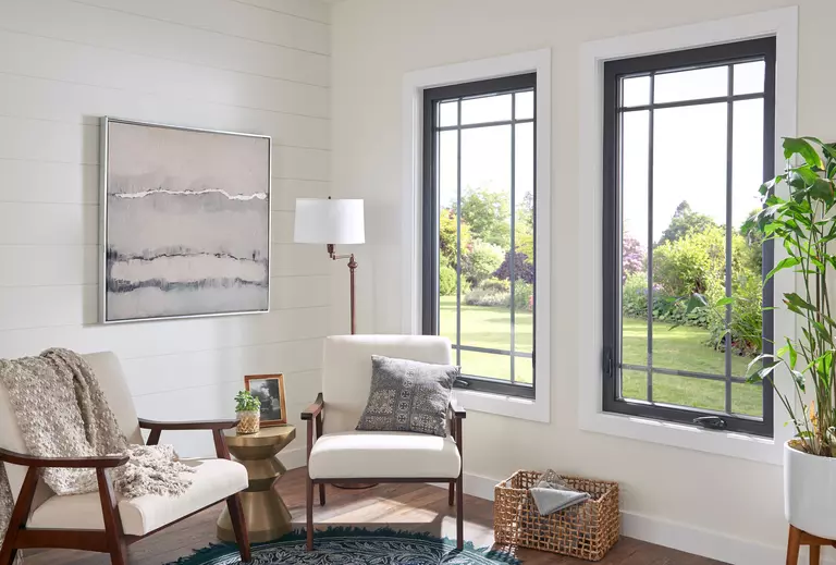 Two upholstered chairs next to black-framed casement windows.