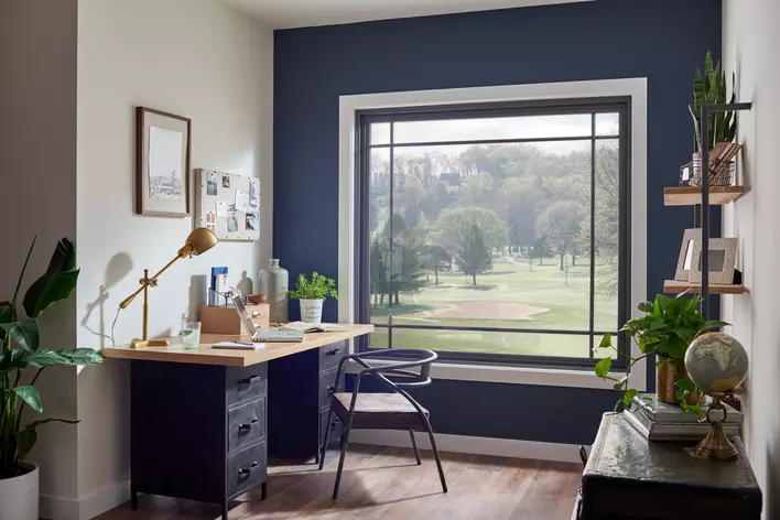A modern decorated in-home office room that is naturally lit from a large picture window overlooking a golf course.