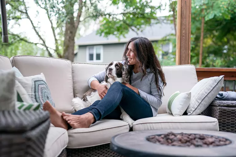 A woman and her dog sitting together on her outdoor furniture on their decorated back patio.