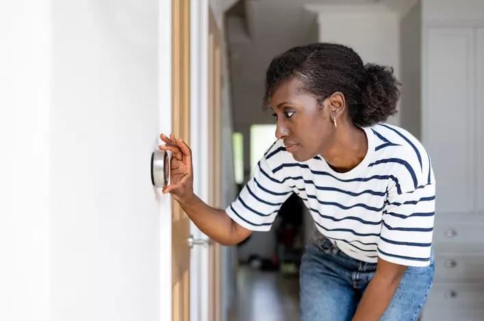 A woman adjusting her thermostat to lower her energy bill