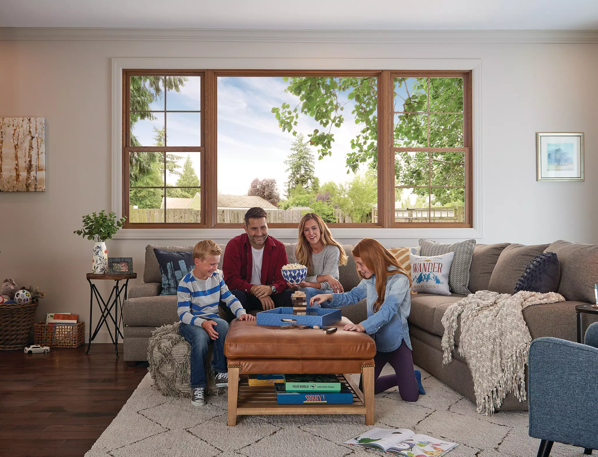 Family playing game on a living room ottoman in front of a large window.