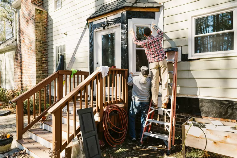 Two workers installing a rectangular window just inside the entryway of a home.