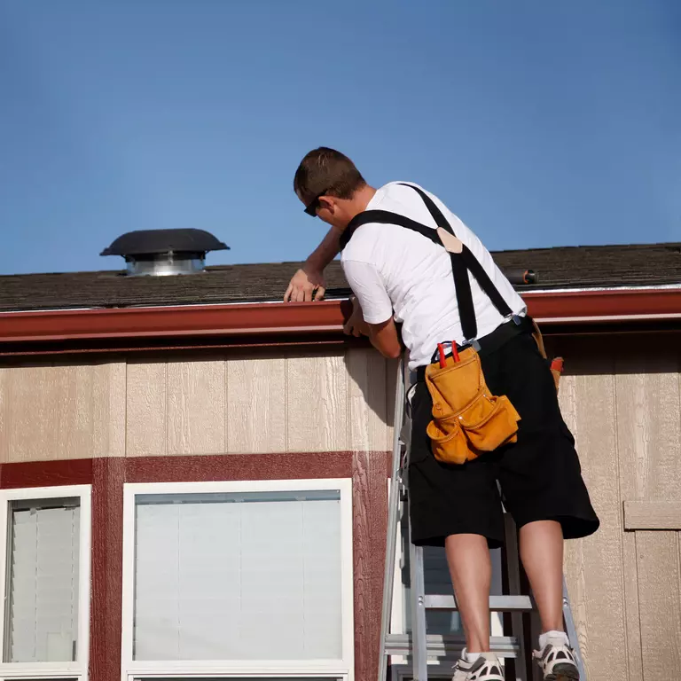 Man atop a ladder on the roof of a home professionally installing a gutter guard system.