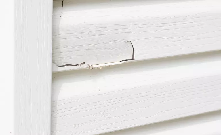 A close-up of cracked white vinyl siding.