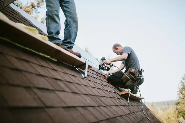 Men on the very top of a home replacing the roof using loud drills and tools to do so. 