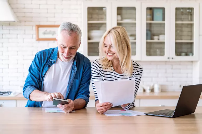 Couple using a smart device and laptop to evaluate their budget.