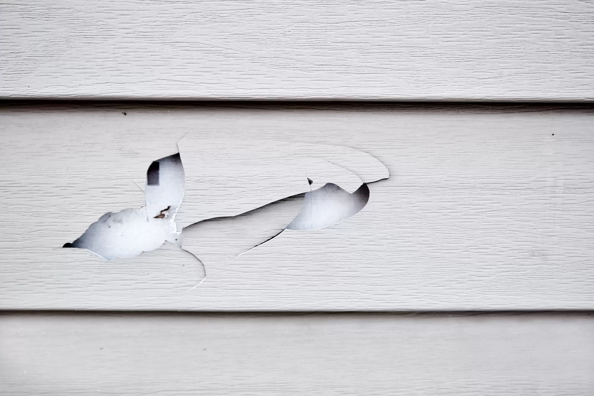 Close-up of a hole in off-white siding.