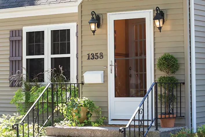 A white full view storm door on a sage green home.