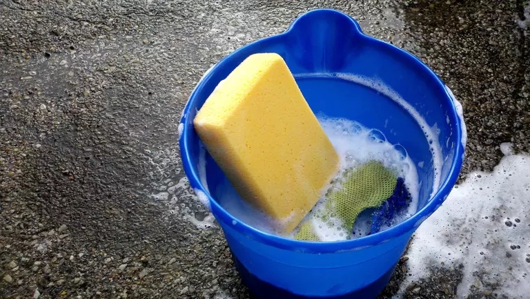 A blue bucket with soap suds and a yellow sponge.