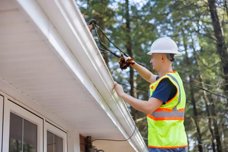 A contractor cleaning the debris out from the gutters of a home to make sure the task is done correctly and safely.